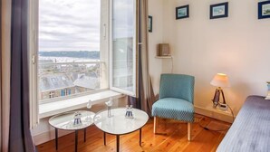 Una habitación con un ventanal grande, una silla, una mesita y una lámpara.