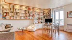 Una sala de estar acogedora con piso de madera, un sofá, una mesa de centro y un comedor con sillas y un televisor.