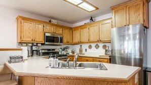 A kitchen with wooden cabinets, a stainless steel refrigerator, a microwave, and a large island with a sink. - Aspen Meadows #2 Sun-Filled, 3 bedroom condo (June Lake)
