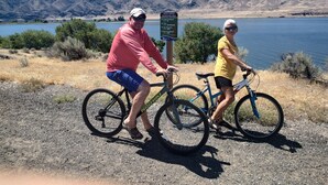 Deux personnes à vélo, près d’un panneau indicateur au bord d’un lac, avec des montagnes en arrière-plan.