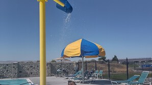 Un espace de jeux aquatiques comprenant une piscine, des chaises longues et un mur de pierre en arrière-plan.