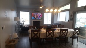 Un coin repas avec une table dressée pour six personnes, un téléviseur fixé au-dessus de la cheminée et un ventilateur de plafond.