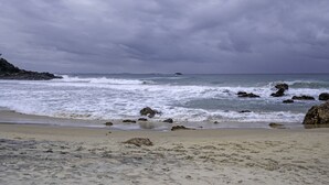 A beach with waves crashing onto the shore, rocky outcrops, and a cloudy sky. - Nobby's 9 - Amazing Ocean Views (Port Macquarie)