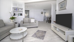 A modern living room with a sofa, coffee table, TV, and a bookshelf. - Nobby's 9 - Amazing Ocean Views (Port Macquarie)