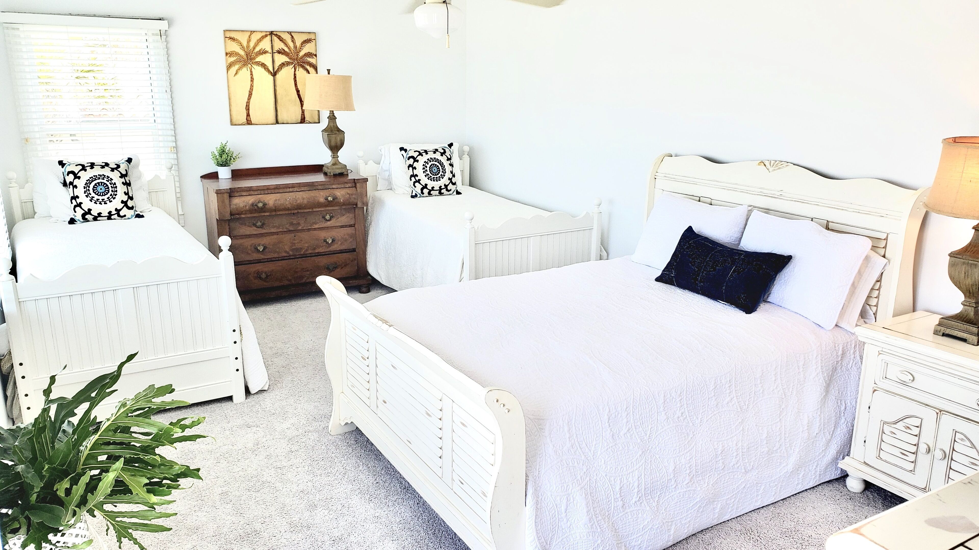 Een slaapkamer in witte tinten met een bed, twee nachtkastjes, een dressoir en een kunstwerk aan de muur.