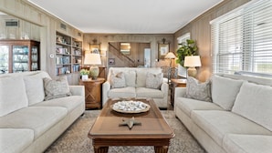 A cozy living room with a beige sofa, a coffee table with decorative items, a bookshelf, and a staircase leading to another level.