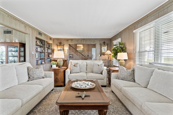A cozy living room with a beige sofa, a coffee table with decorative items, a bookshelf, and a staircase leading to another level.
