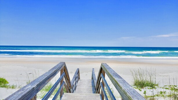 A wooden boardwalk leading to a beach with waves in the background.
