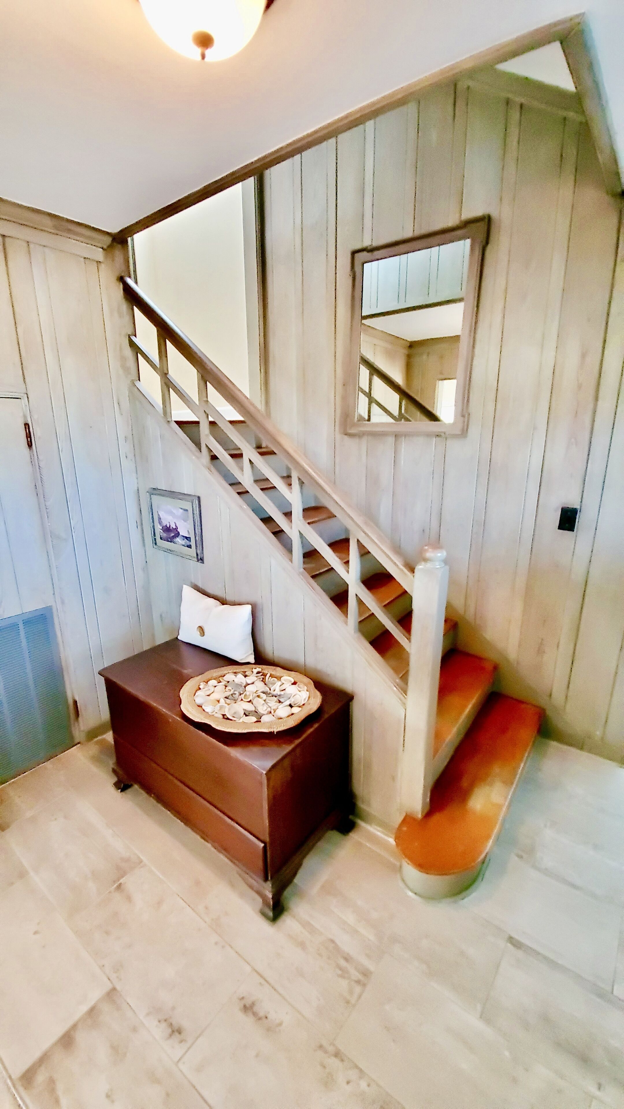 A wooden staircase with a handrail, a small table with a cushion, and a mirror on the wall.