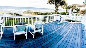 A wooden deck with white railings and four chairs facing the ocean.