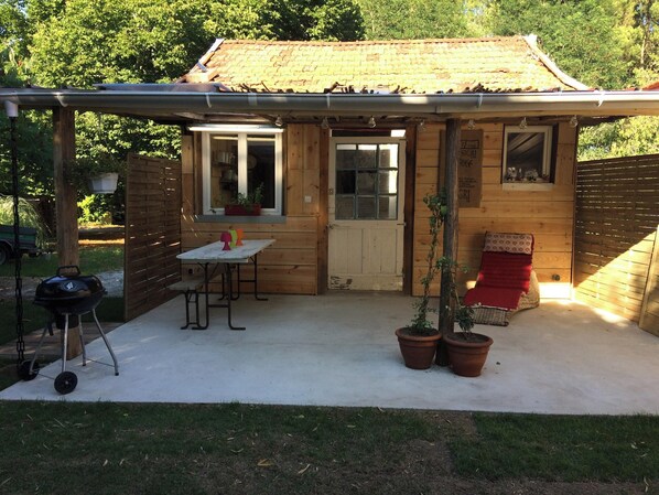 Eine Holz-Blockhütte mit überdachter Terrasse, Grill und Blumentöpfen.