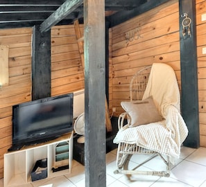 L’intérieur d’un chalet en bois, avec un téléviseur posé sur un meuble, un fauteuil à bascule recouvert d’une couverture et des murs en bois.