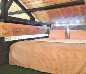 Ein Stockbett mit einem Holz-Kopfteil, einem grünen Teppichboden und einer schrägen Decke mit freiliegenden Balken.