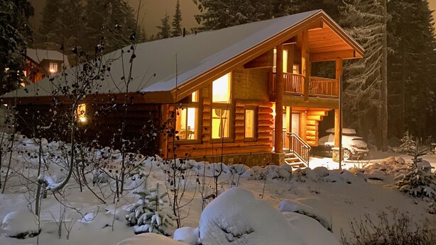 Una cabaña de troncos con balcón, rodeada de árboles cubiertos de nieve.