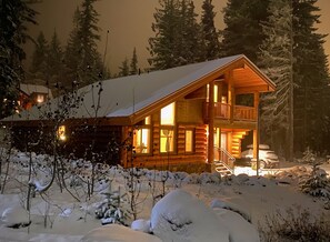 Una cabaña de troncos con balcón, rodeada de árboles cubiertos de nieve.