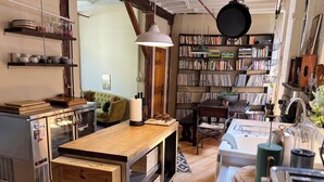 A cozy kitchen with wooden countertops, a hanging pot rack, and a bookshelf filled with books.