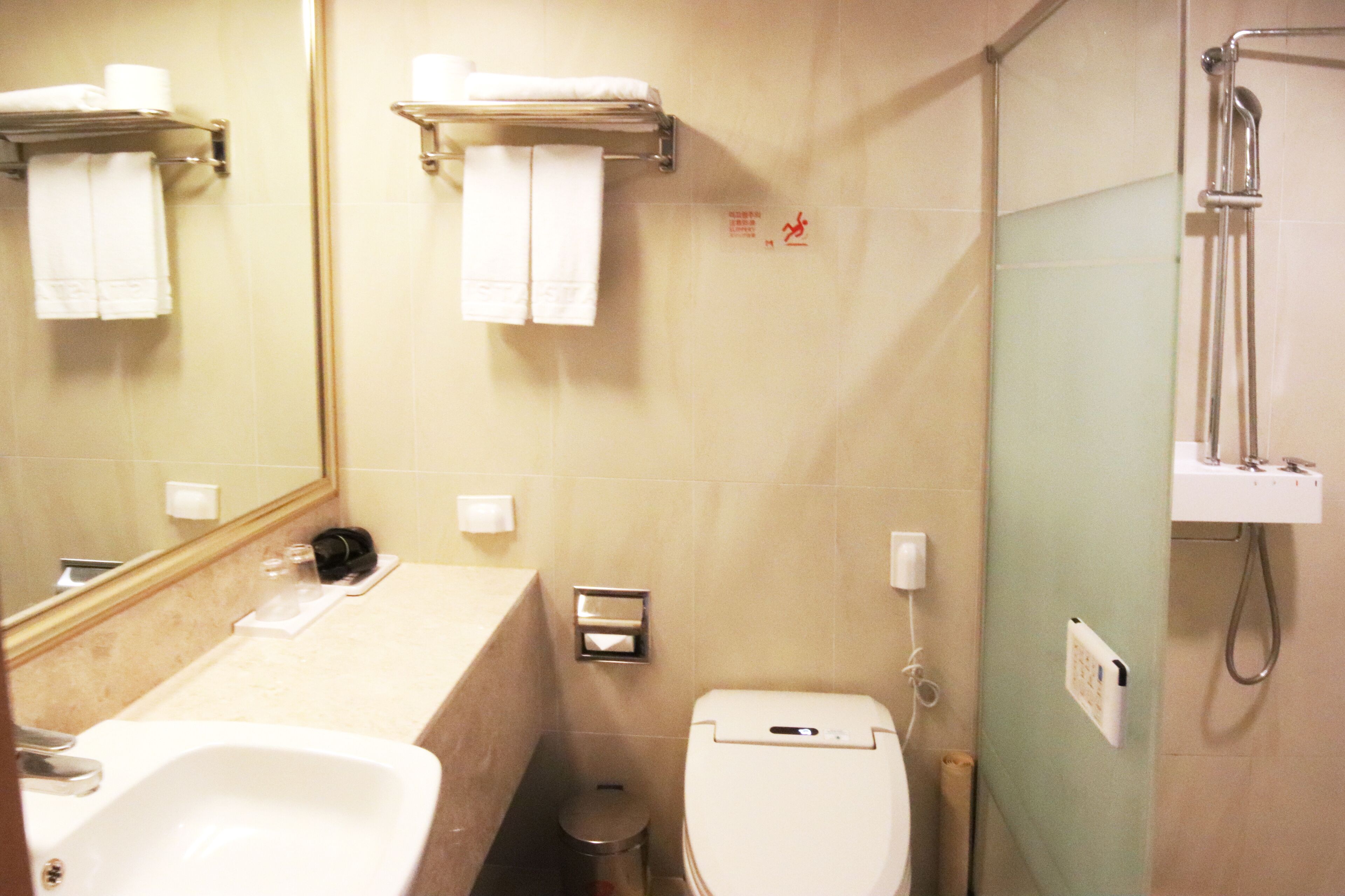 Un baño con lavamanos, inodoro y ducha. Hay toallas colgadas en un perchero y un cubo de basura.