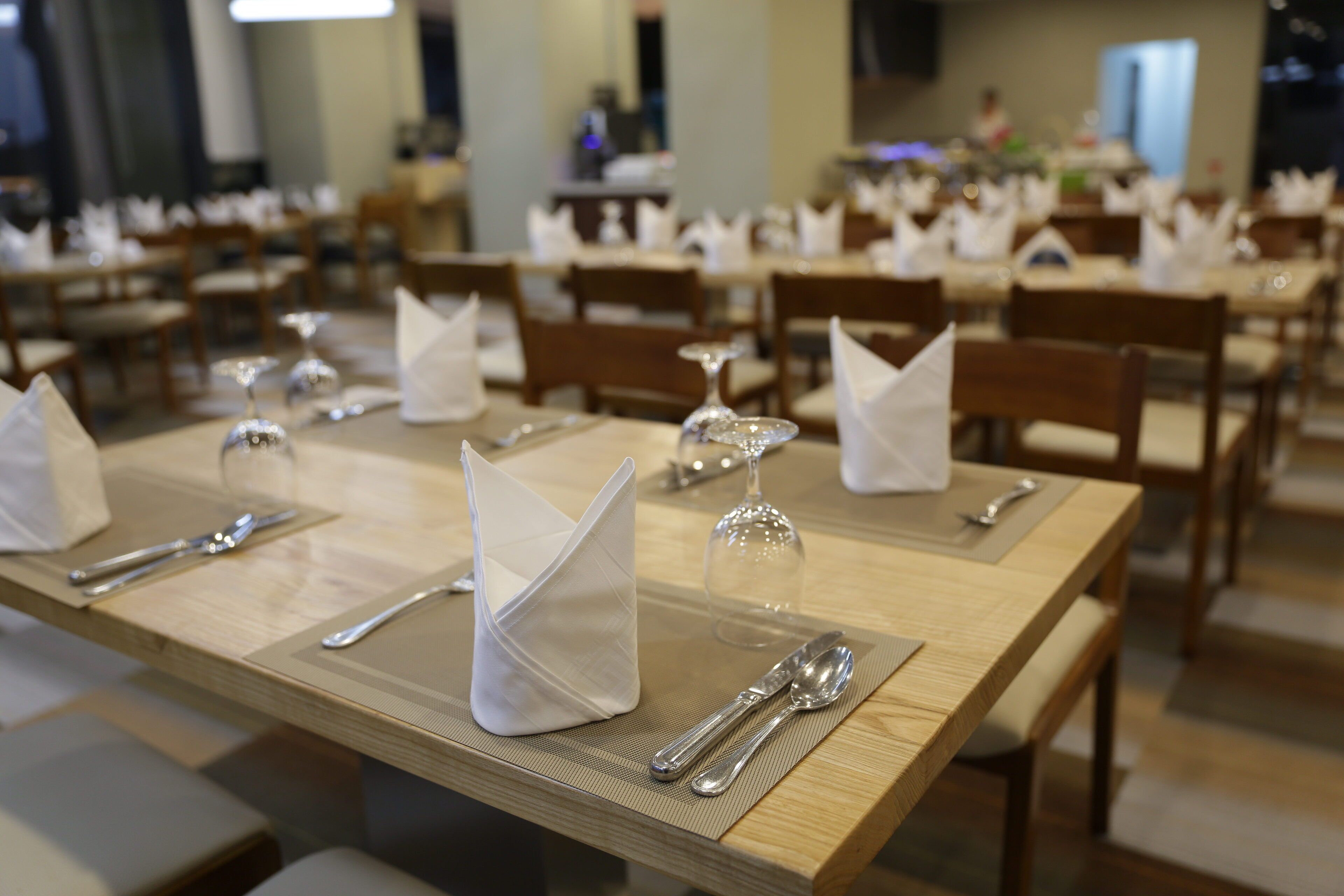 A dining area with neatly set tables, each with cutlery, glasses, and napkins.