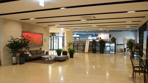 Un hall d’entrée spacieux au design moderne, comprenant un coin salon avec des canapés et une table basse, des plantes en pot, et offrant une vue dégagée sur le comptoir de réception en arrière-plan.