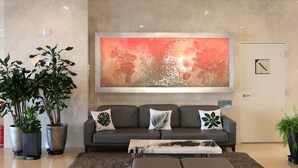 Un hall d’entrée moderne avec un canapé gris, des plantes en pot et un grand tableau abstrait accroché au mur.