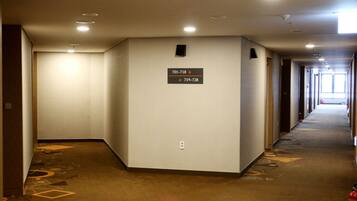A hotel corridor with a carpeted floor, a sign indicating room numbers, and a fire extinguisher on the right.