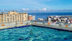 Une piscine à l’eau d’un bleu cristallin, entourée de bâtiments et offrant une vue sur la mer.