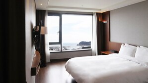 Une chambre d’hôtel avec un grand lit, une table de chevet, un bureau et une fenêtre donnant sur la mer et une falaise.