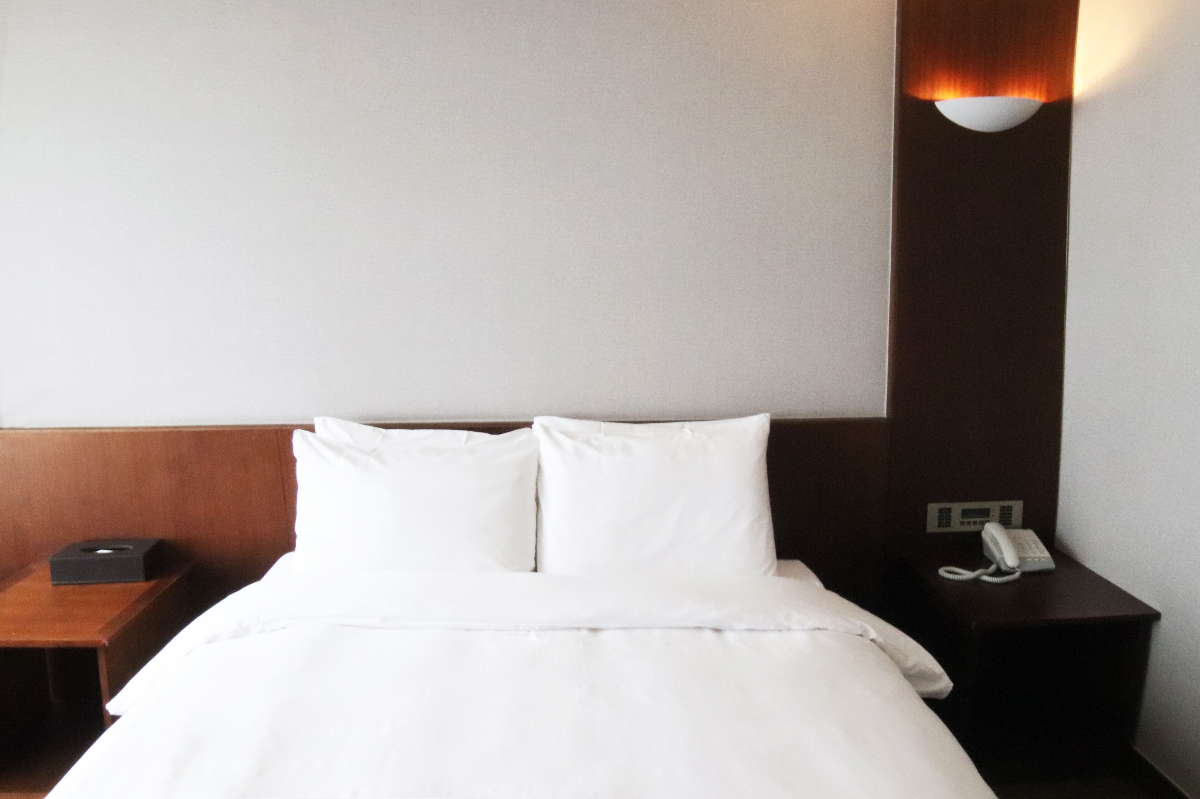Habitación de hotel con una cama bien hecha, una mesita de noche con teléfono y una lámpara de pared.