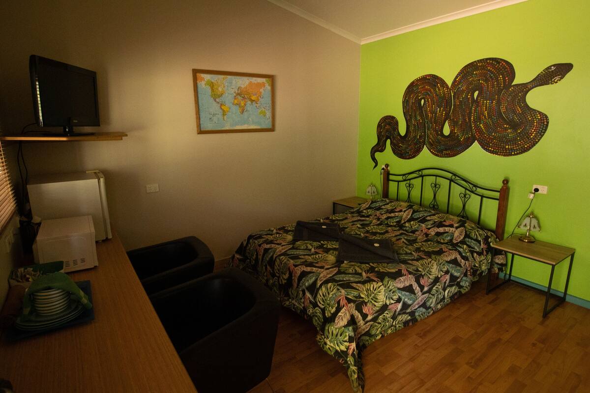 Une chambre à coucher avec un lit, une carte accrochée au mur, un serpent décoratif et un téléviseur posé sur une étagère.