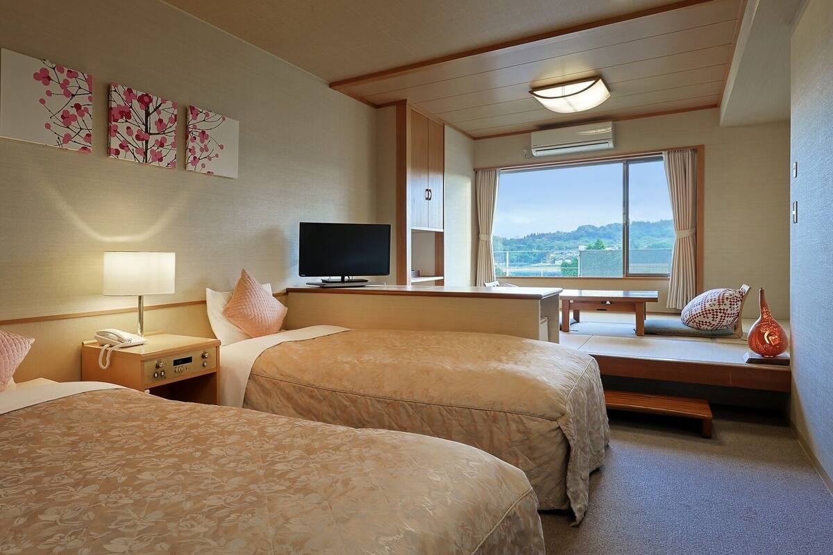 Habitación de hotel con dos camas, televisor, escritorio y ventana con vista a la ciudad.