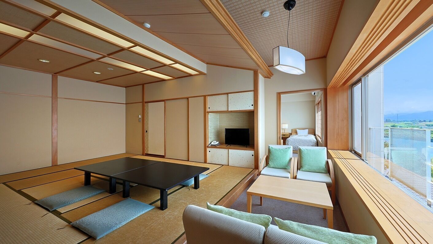 Ein Zimmer mit Tatami-Böden, einem niedrigen Tisch, einer Couch, einem Fernseher und einem großen Fenster mit Blick.