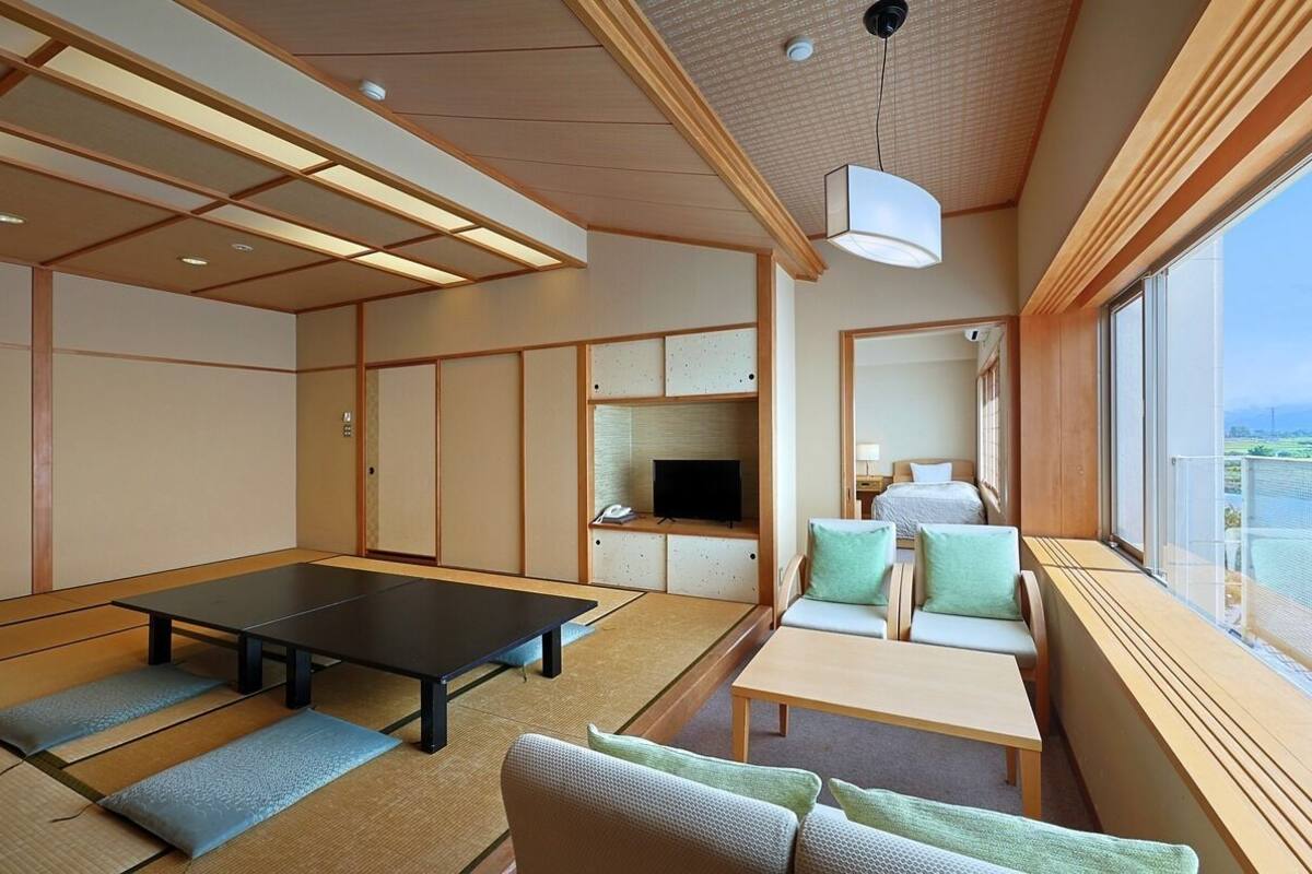 Una habitación con suelo de tatami, una mesa baja, un sofá, un televisor y un ventanal con vistas.