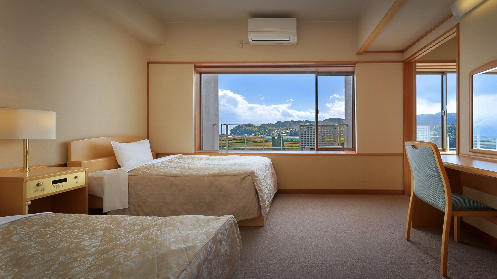 Une chambre d’hôtel avec deux lits, un bureau, une chaise et une grande fenêtre donnant sur le paysage.