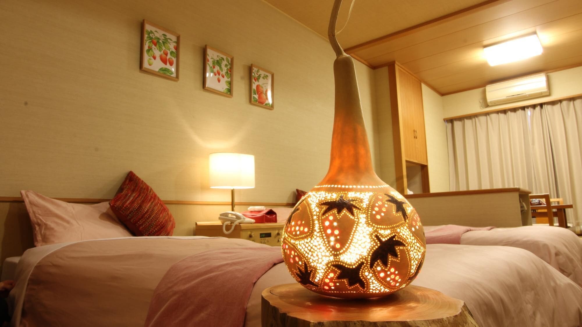 A hotel room with two beds, a bedside lamp, and a decorative vase on a wooden stool.