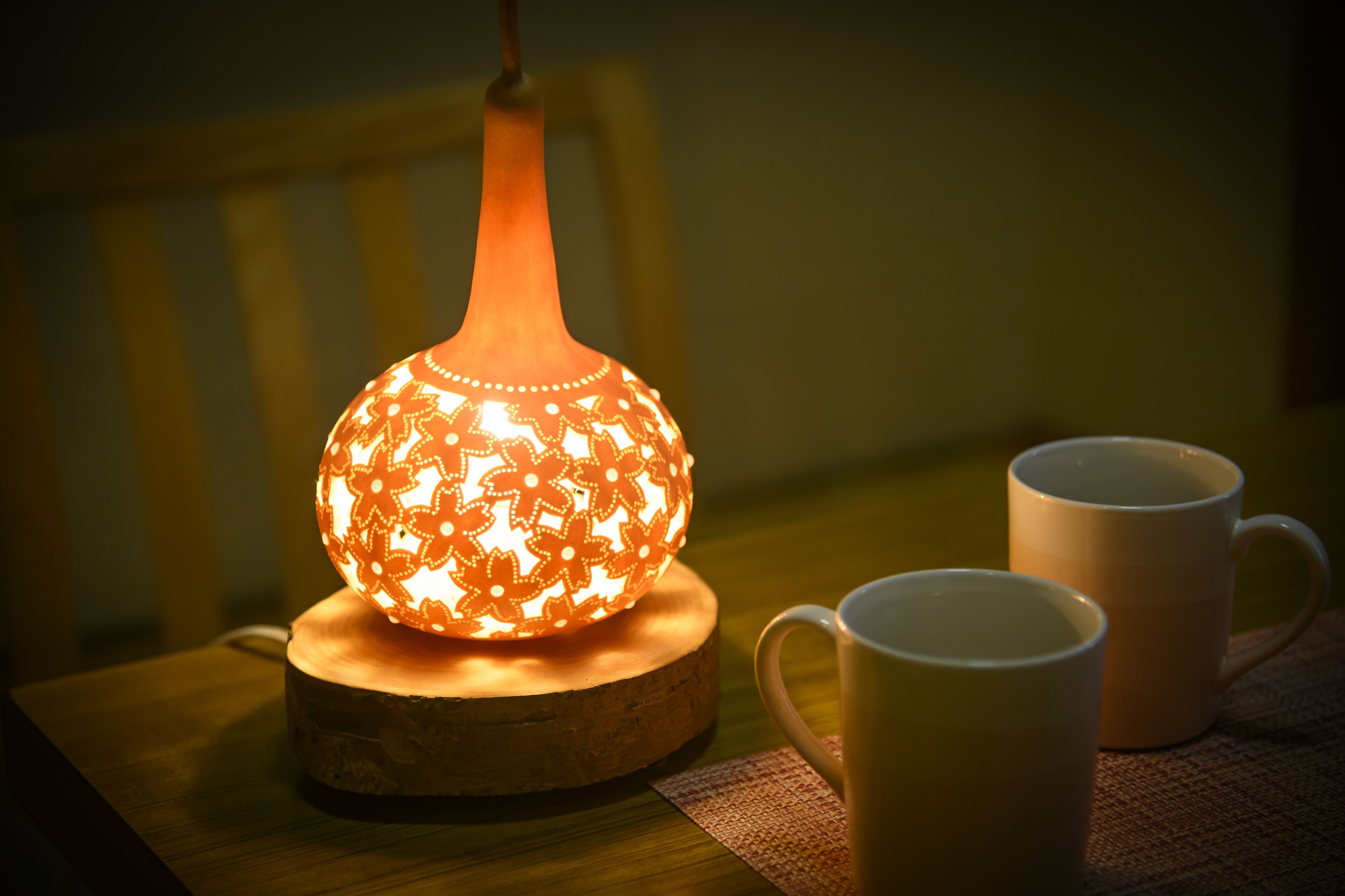 A table with a decorative lamp, two white mugs, and a wooden coaster.