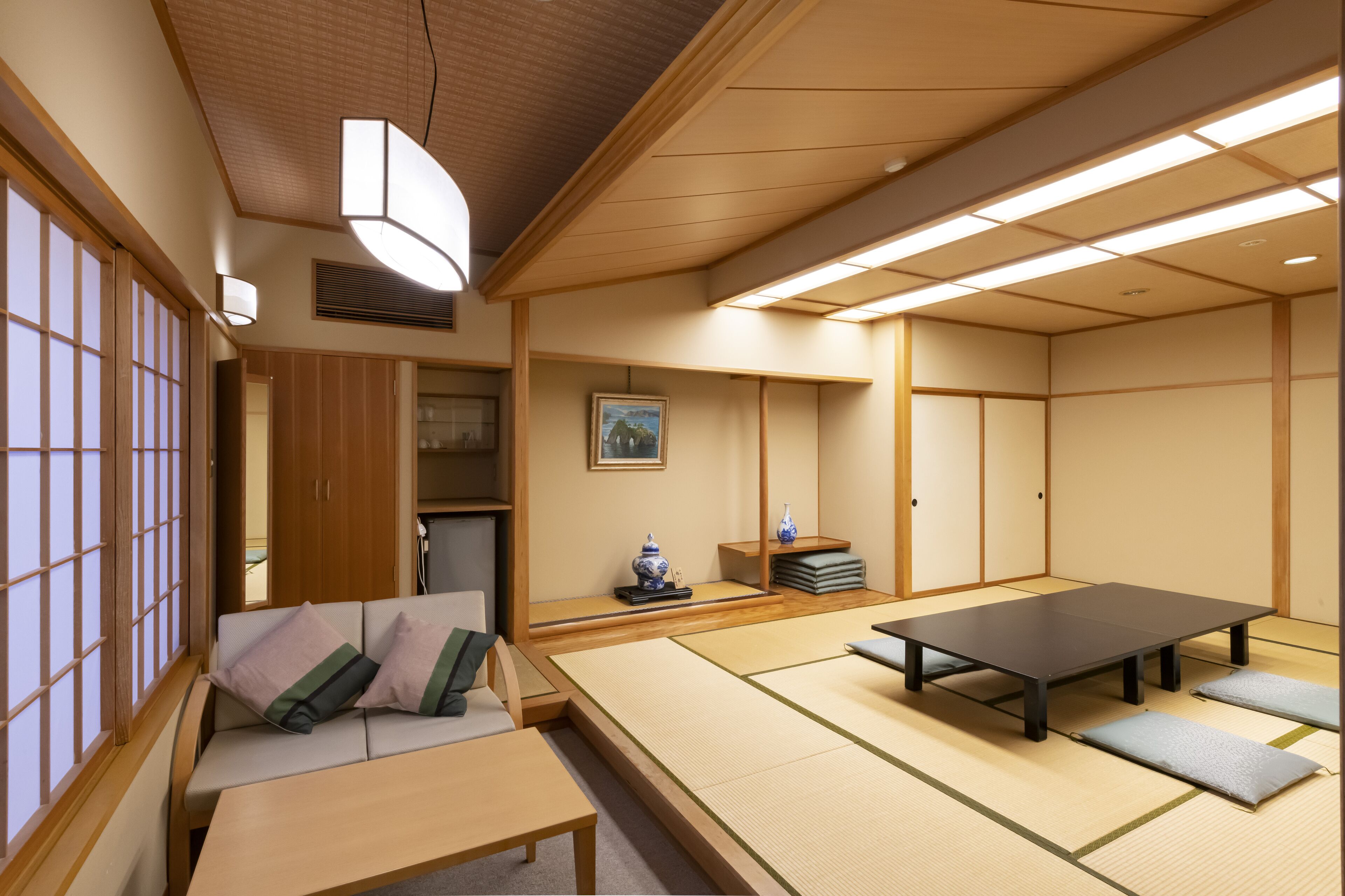Et traditionelt japansk rum med tatamimåtter, et lavt bord, en sofa med hynder, skydedøre og et loft med indbygningsbelysning.