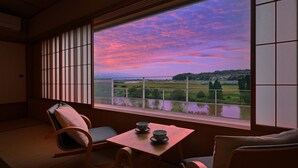 Una habitación japonesa tradicional con suelo de tatami, una mesa baja con dos cuencos y vistas a un paisaje al atardecer.