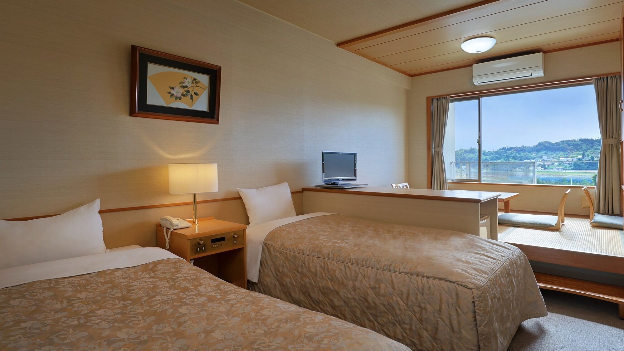Ein Hotelzimmer mit zwei Betten, einem Schreibtisch mit Computer, einem Fernseher, einem Telefon und einem Fenster mit Aussicht.