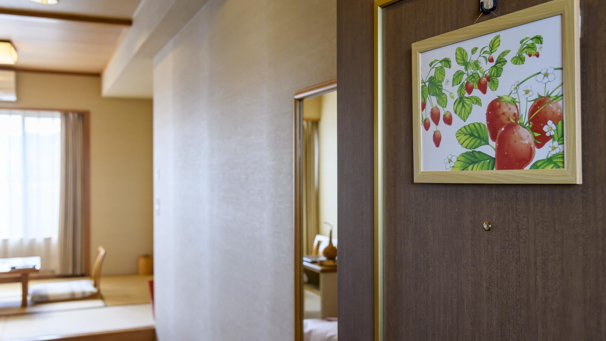 A hotel room with a wooden door, a framed picture of strawberries, a bed, and a window with curtains.