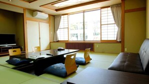 A traditional Japanese-style living room with tatami flooring, a low table, cushions, and a sofa. - Hotel Symphony (Sagae)