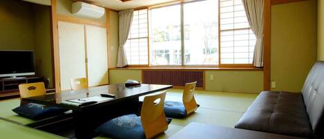 Una sala de estar tradicional japonesa con suelo de tatami, una mesa baja, cojines y un sofá.