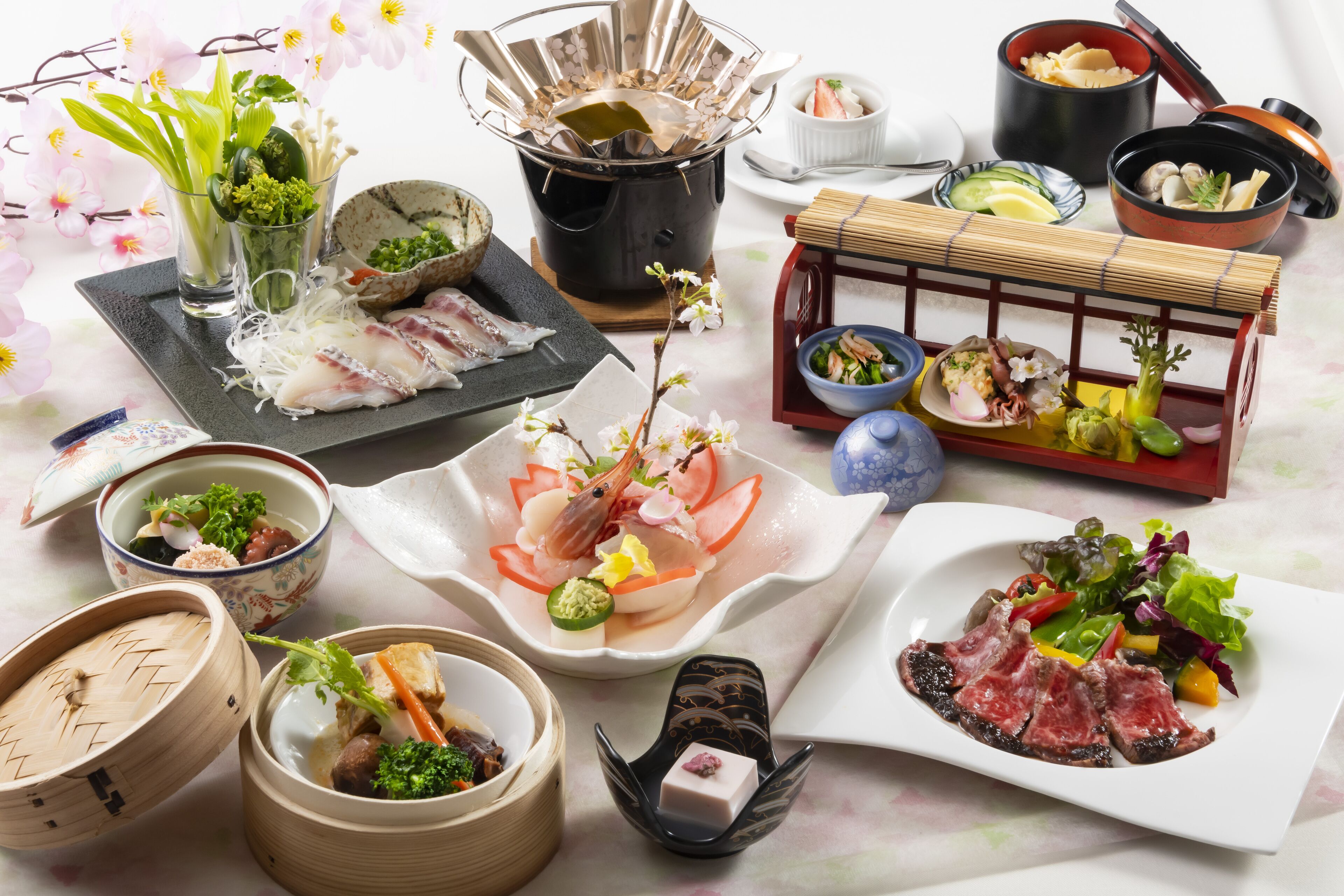 A variety of dishes including sashimi, vegetables, and a meat dish, arranged on a table with decorative elements like flowers and traditional containers.