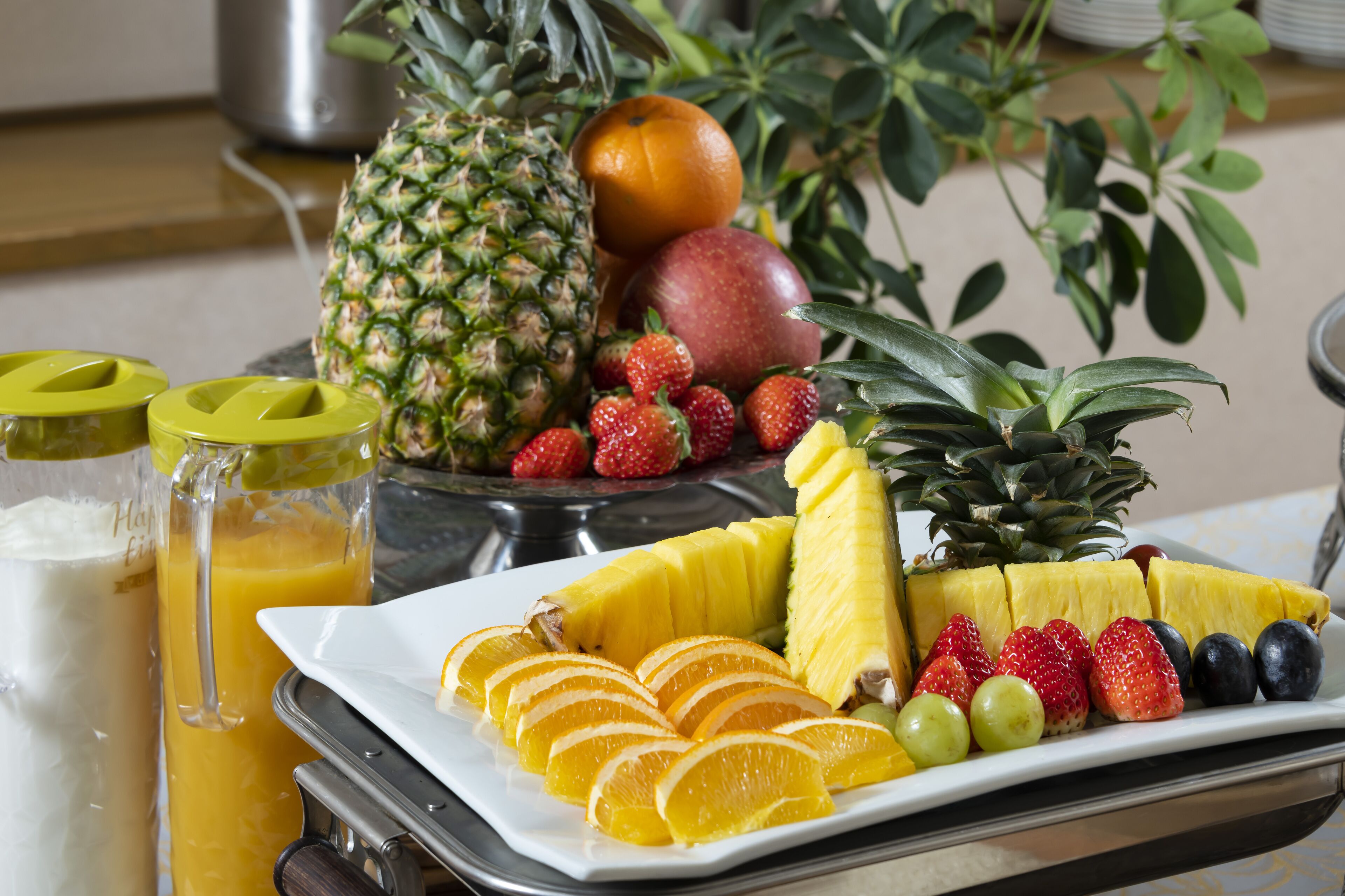A breakfast tray with fruits, a pineapple, a banana, and a glass of orange juice.