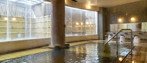 Una piscina interior con paredes de vidrio transparente, una columna central y suelo de baldosas.