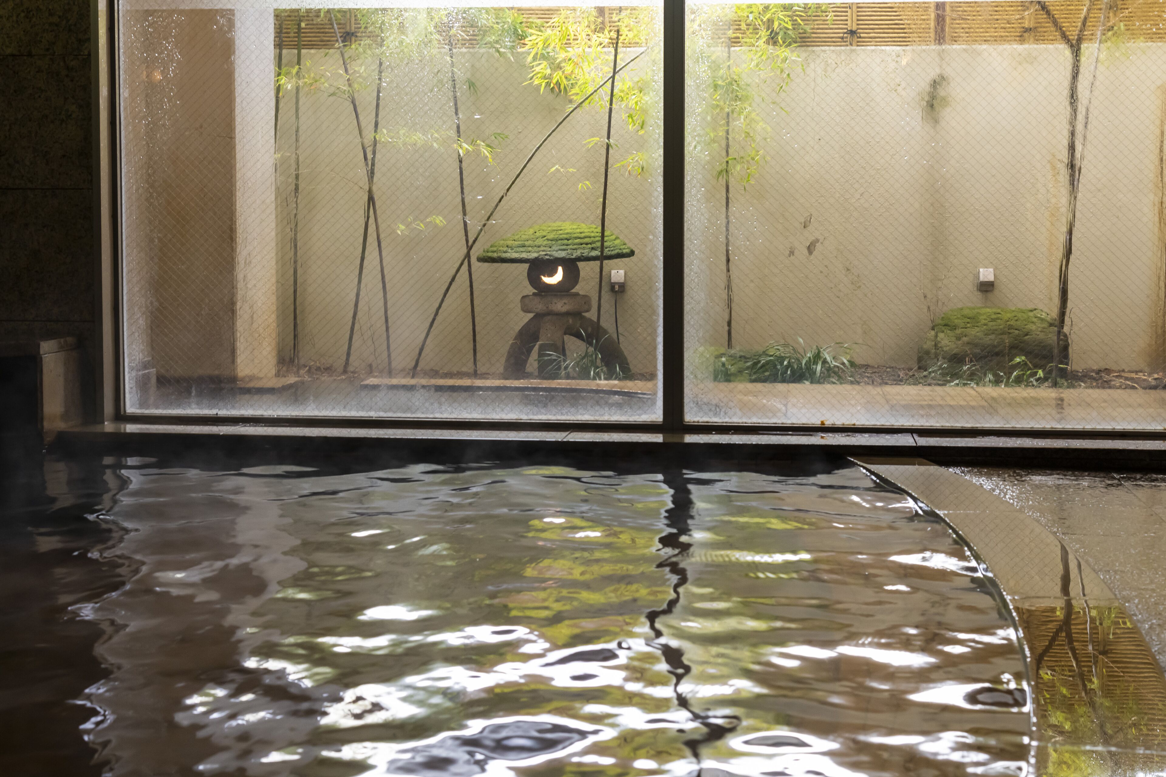 Vista a través de una ventana que da a una habitación con una fuente de agua y una estructura de piedra.