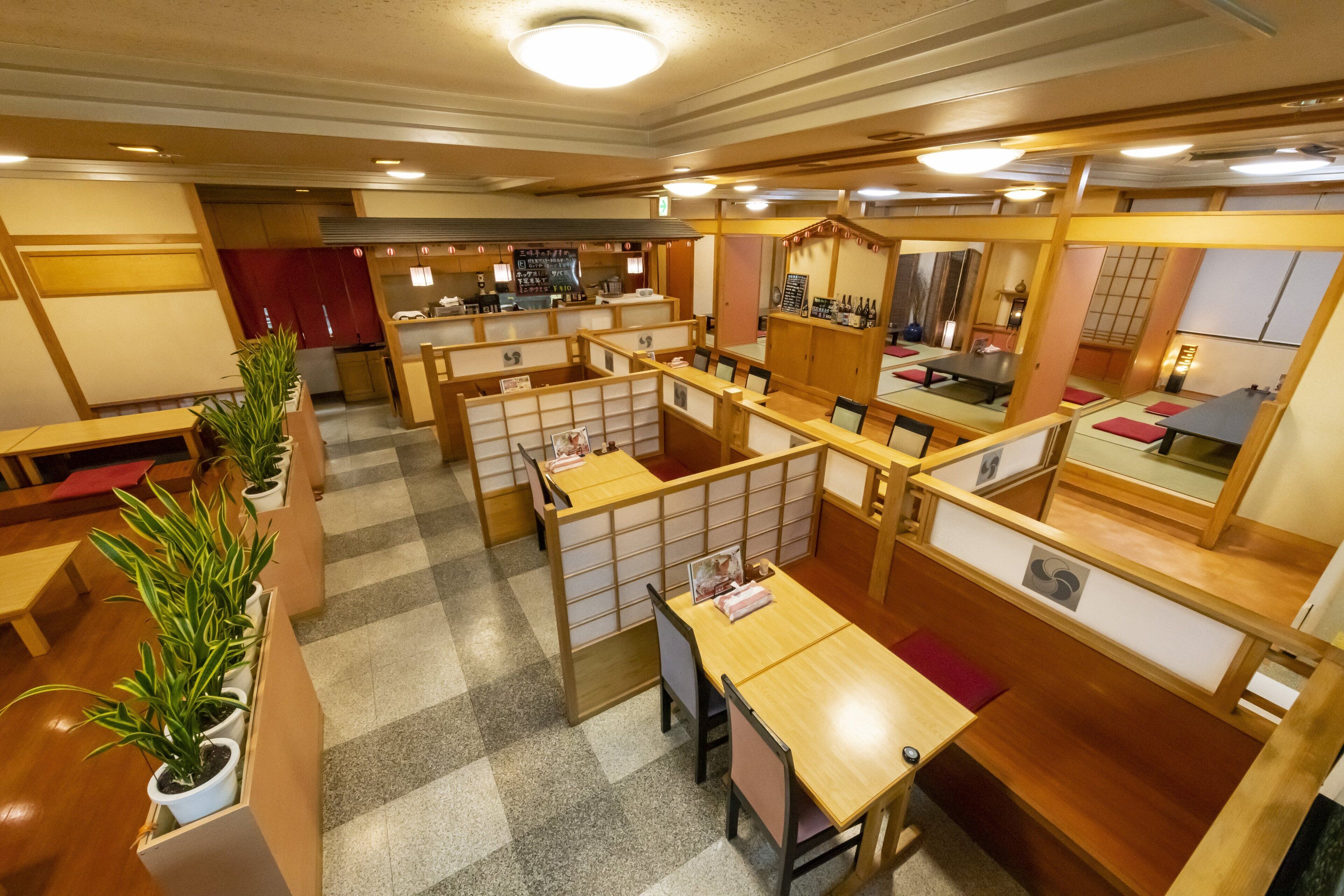 A traditional Japanese restaurant with wooden partitions, tatami mats, and potted plants.
