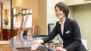 A reception desk with a computer, a name tag, and a plant in the background. - Hotel Symphony (Sagae)