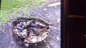 Un foyer extérieur en métal, avec des bûches et du petit bois.