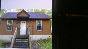 Une petite maison en bois avec une porte blanche, deux fenêtres et un petit porche doté d’un escalier en bois.