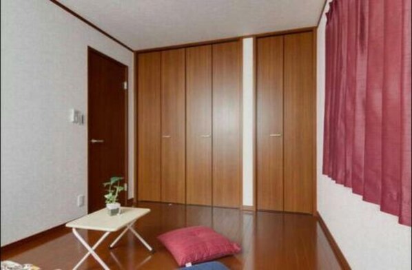 A room with a wooden wardrobe, a small table with a plant, and a red cushion on the floor. - Tammy Hostel Villa (Osaka)